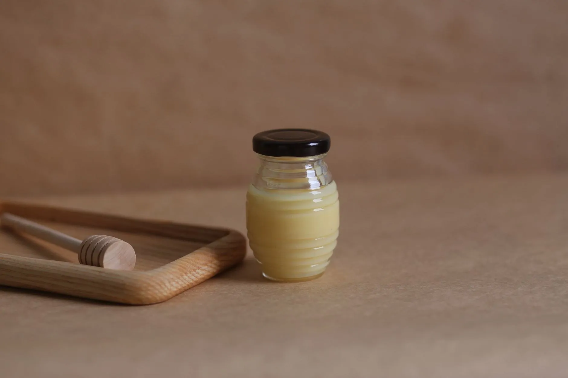 A jar of pale, creamy soft-set honey beside an oak tray and dipper