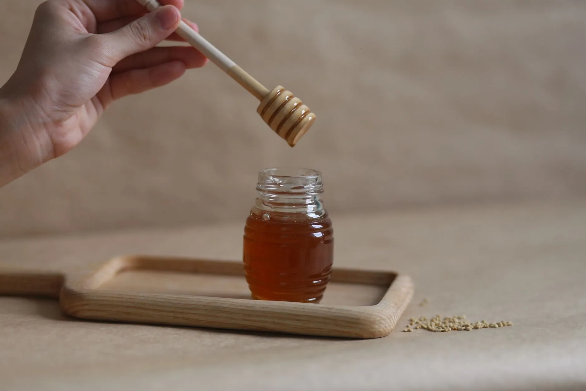 A dipper lifted over a small jar of dark amber heather honey on an oak tray