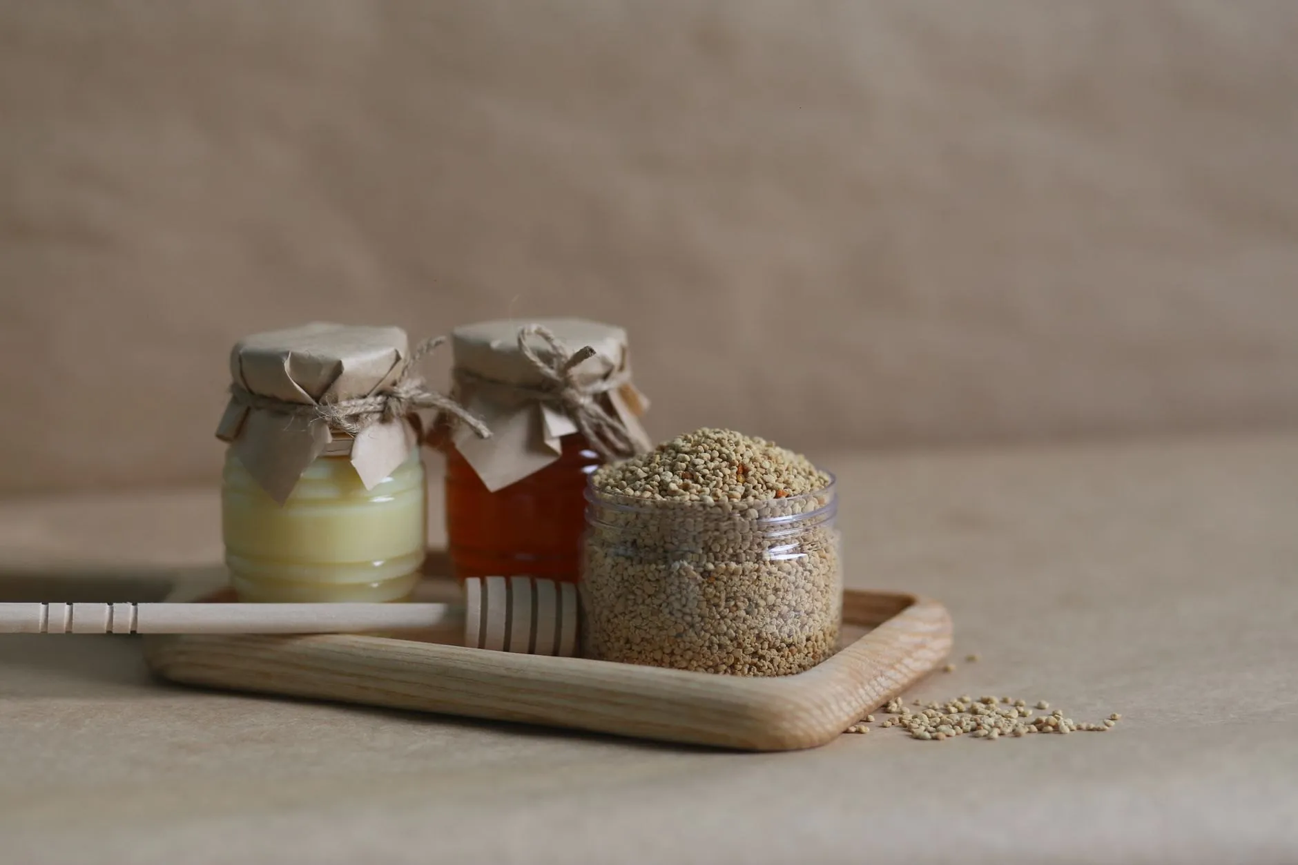 Three jars on an oak tray, two of honey and one of golden bee pollen, with a dipper