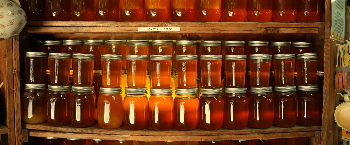 Jars of honey on wooden shelves, each a different colour.